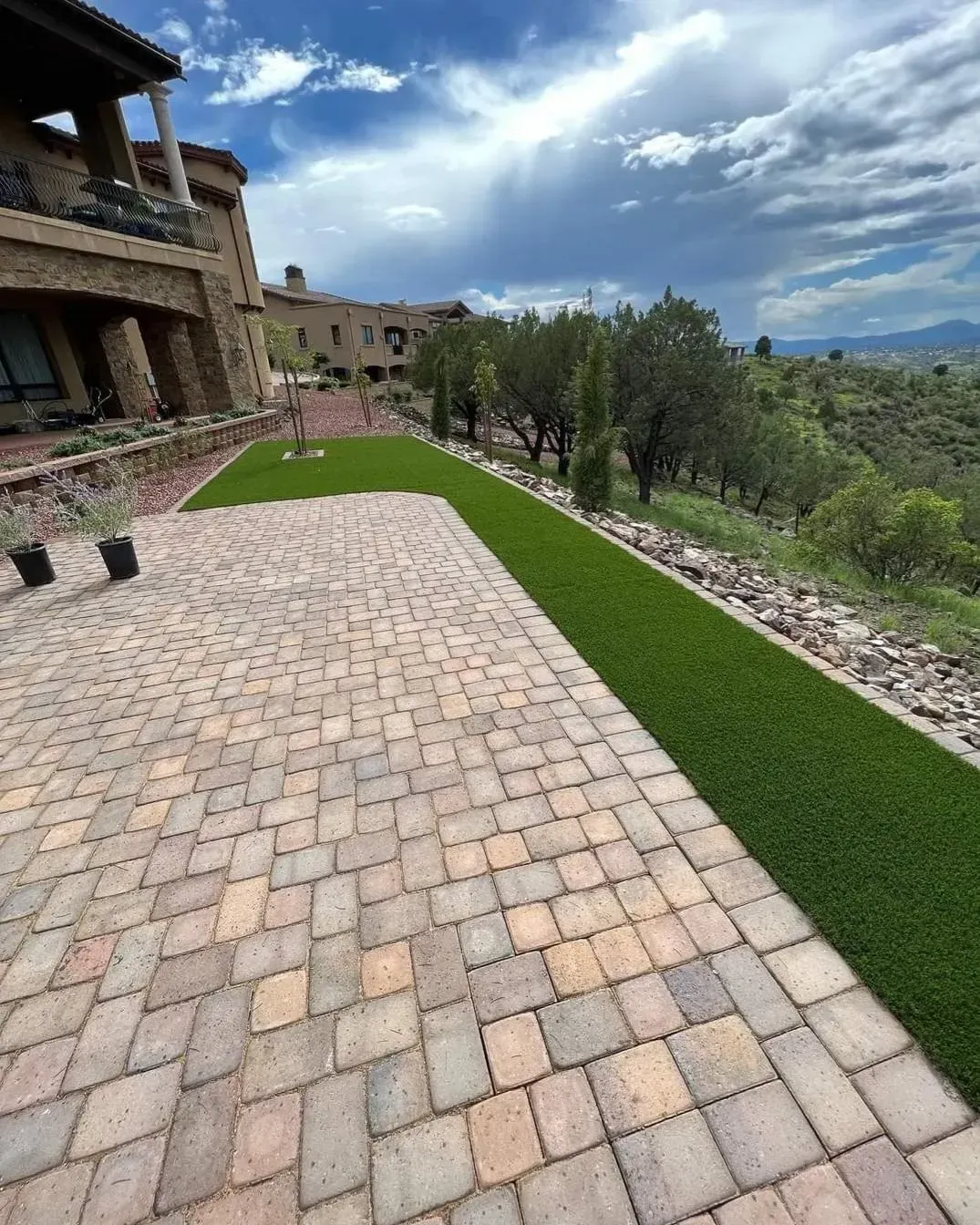 A brick patio with a lush green lawn in front of a large house.