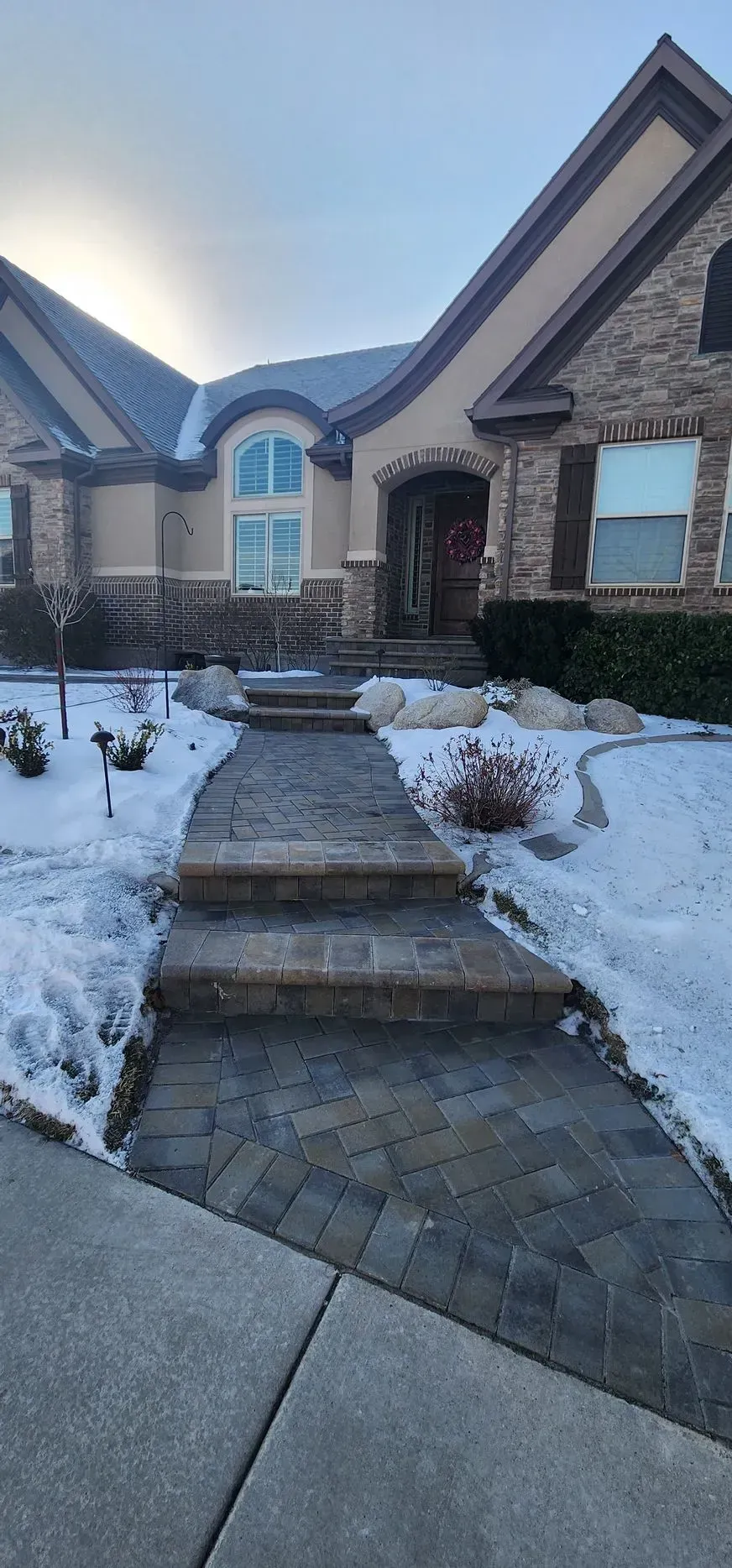 A stone walkway leading to a large house covered in snow.