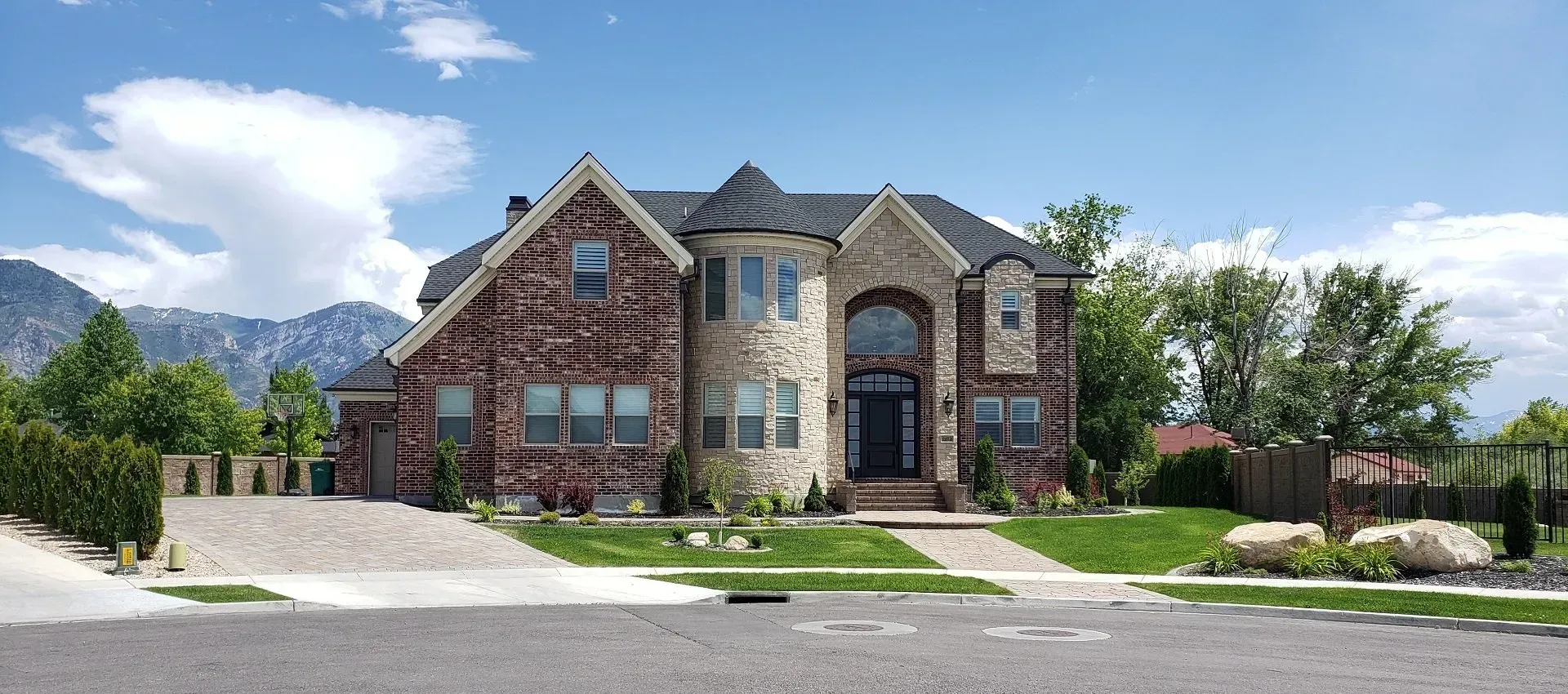 A large brick house with mountains in the background is sitting on top of a lush green hillside.