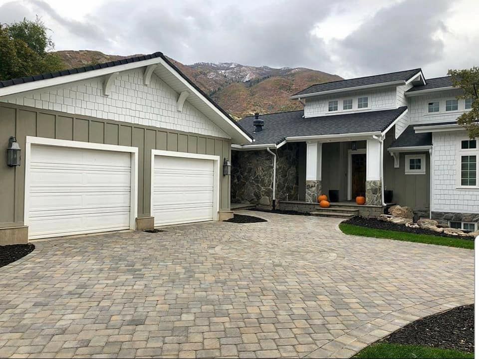 A large white house with two garage doors and a brick driveway.