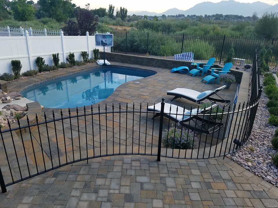 A fence surrounds a large swimming pool with chairs around it