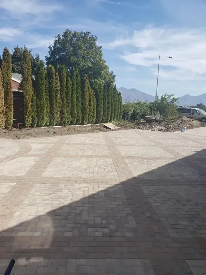 A brick driveway with a fence and trees in the background