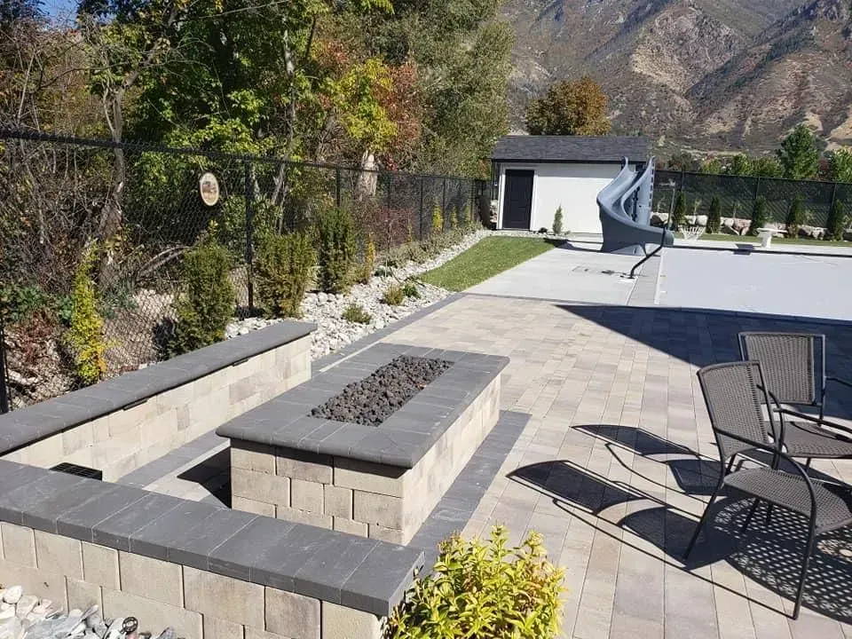 A fire pit is in the middle of a patio next to a pool.