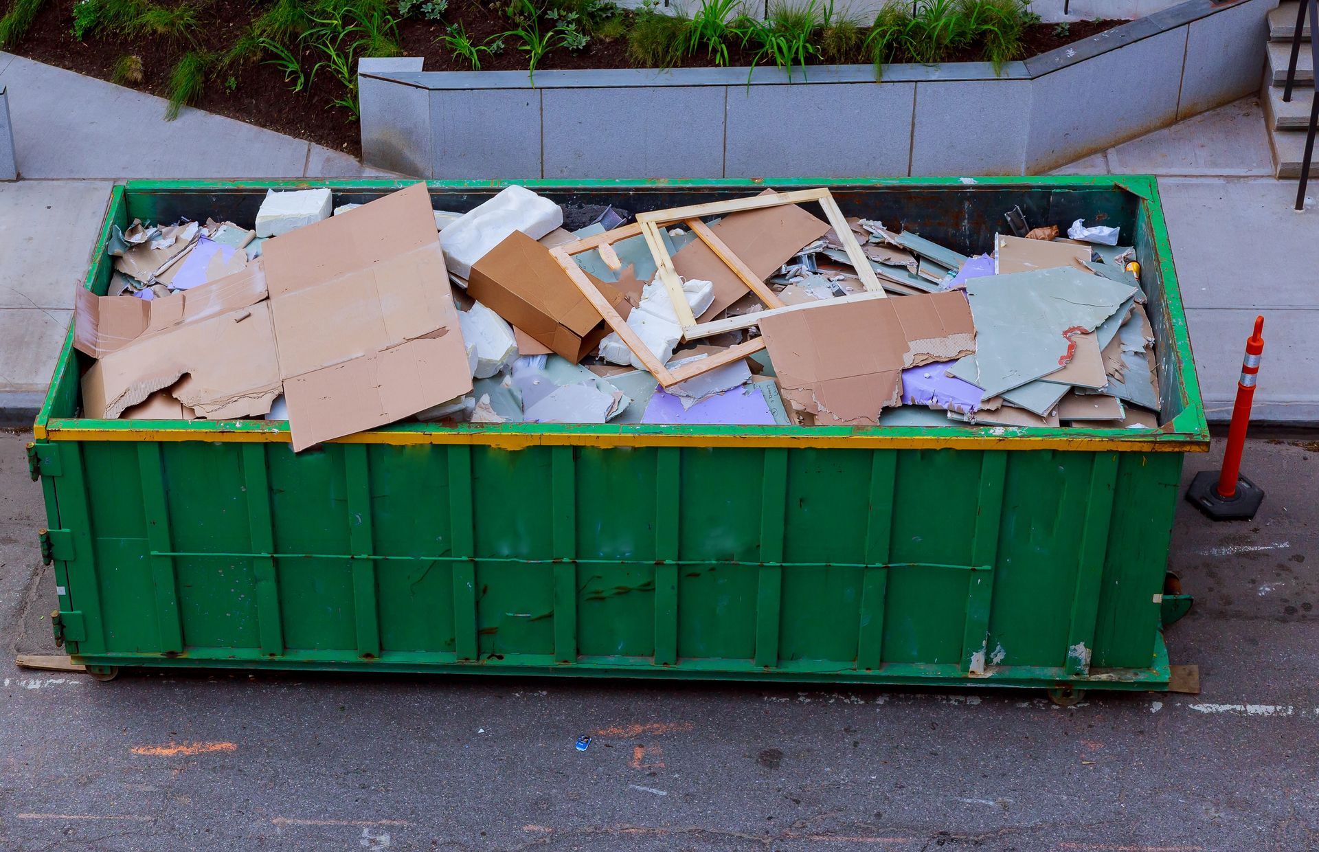 Green dumpster overflowing with construction debris on a city street.