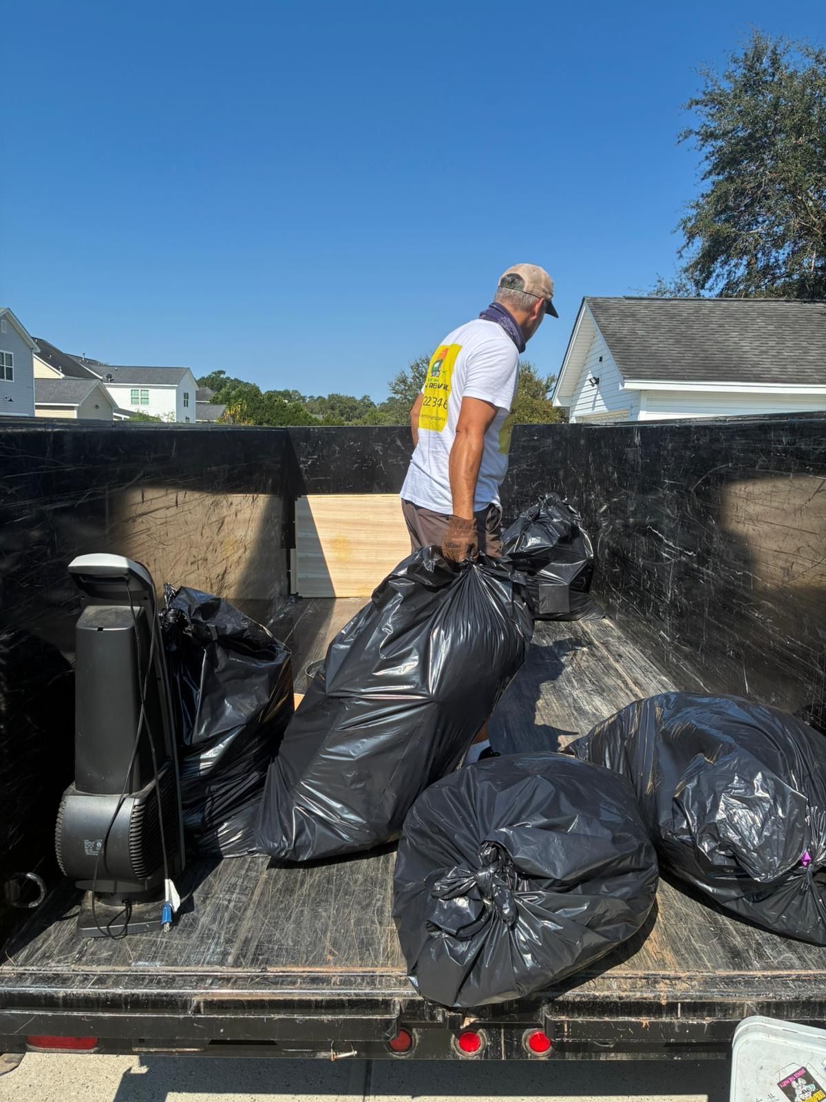 Man loading black trash bags into a truck bed on a sunny day.