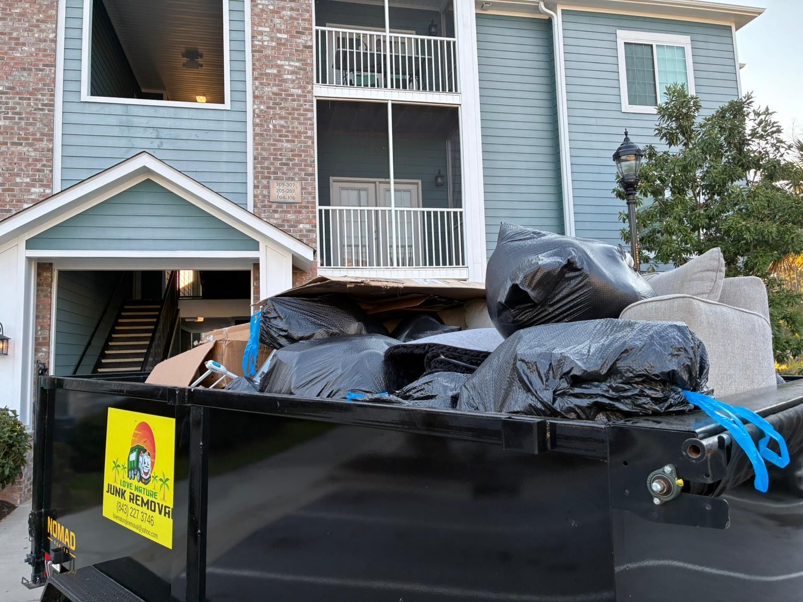 Dumpster overflowing with trash in front of a blue apartment building.