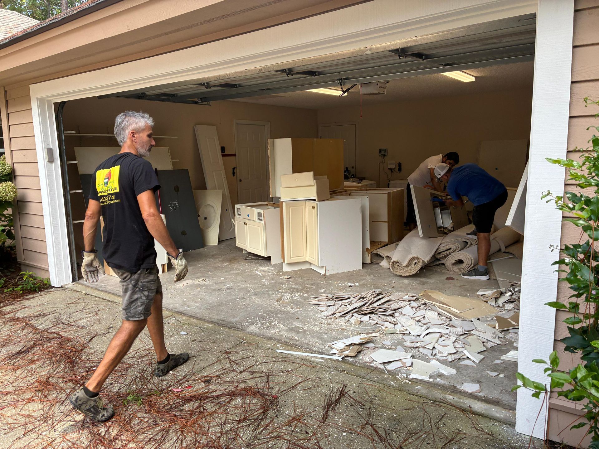 Men clearing debris and cabinetry from a damaged garage, with open door.