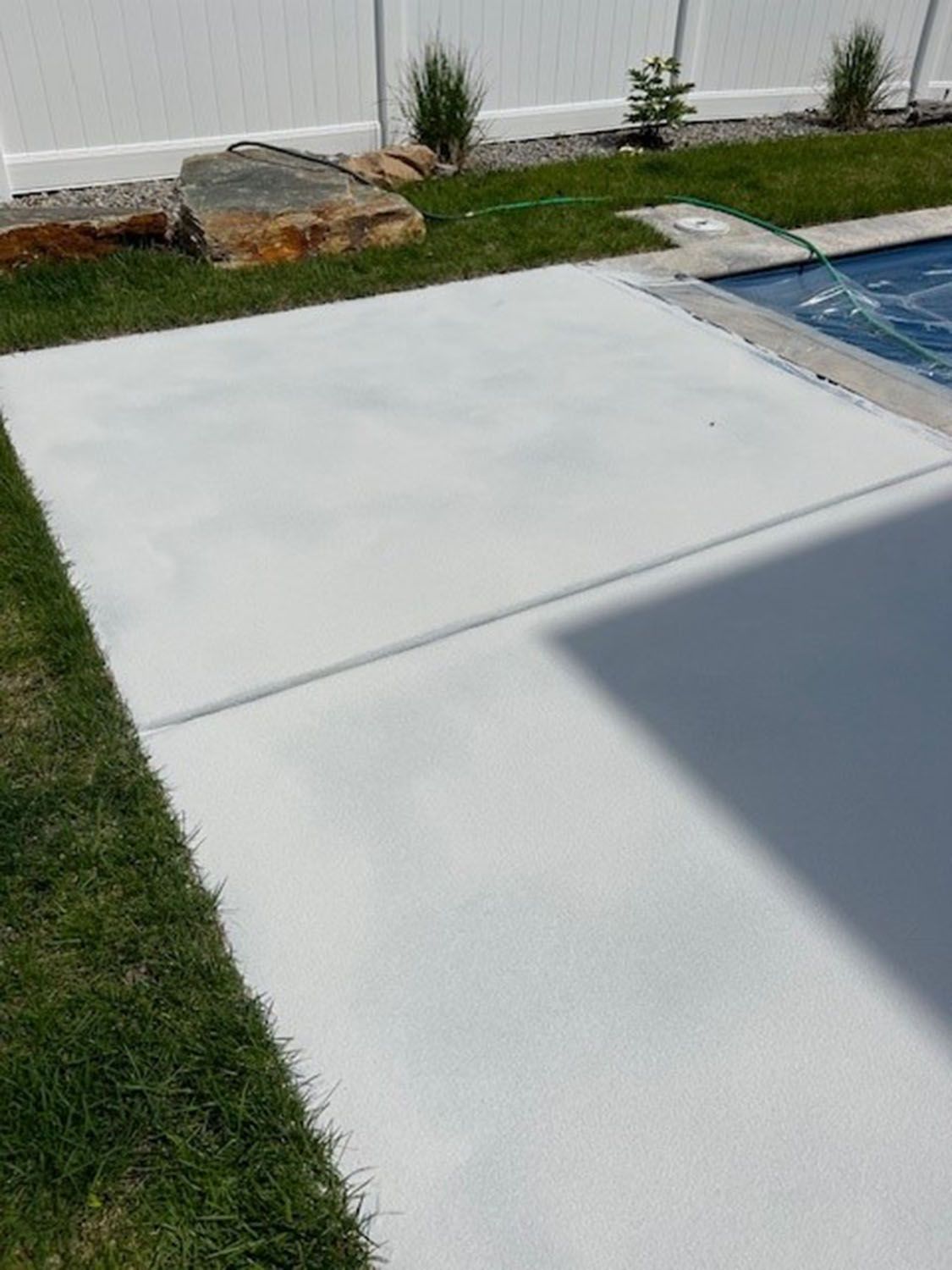 a concrete walkway next to a swimming pool with a white fence in the background