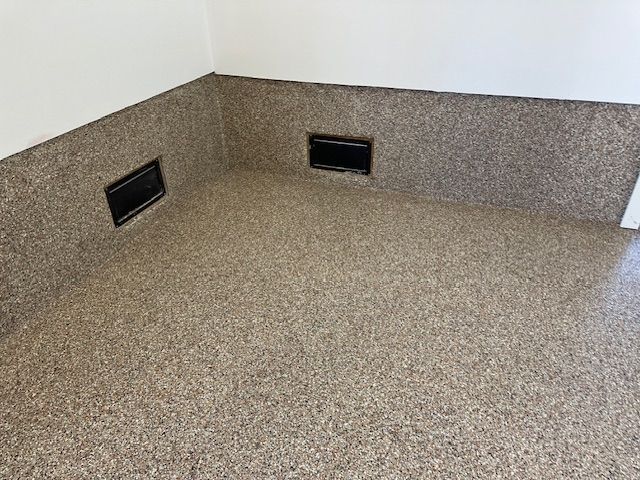 A corner of a room with a concrete floor and a white wall