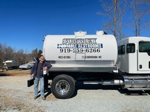 A man is standing next to a portable restrooms truck.