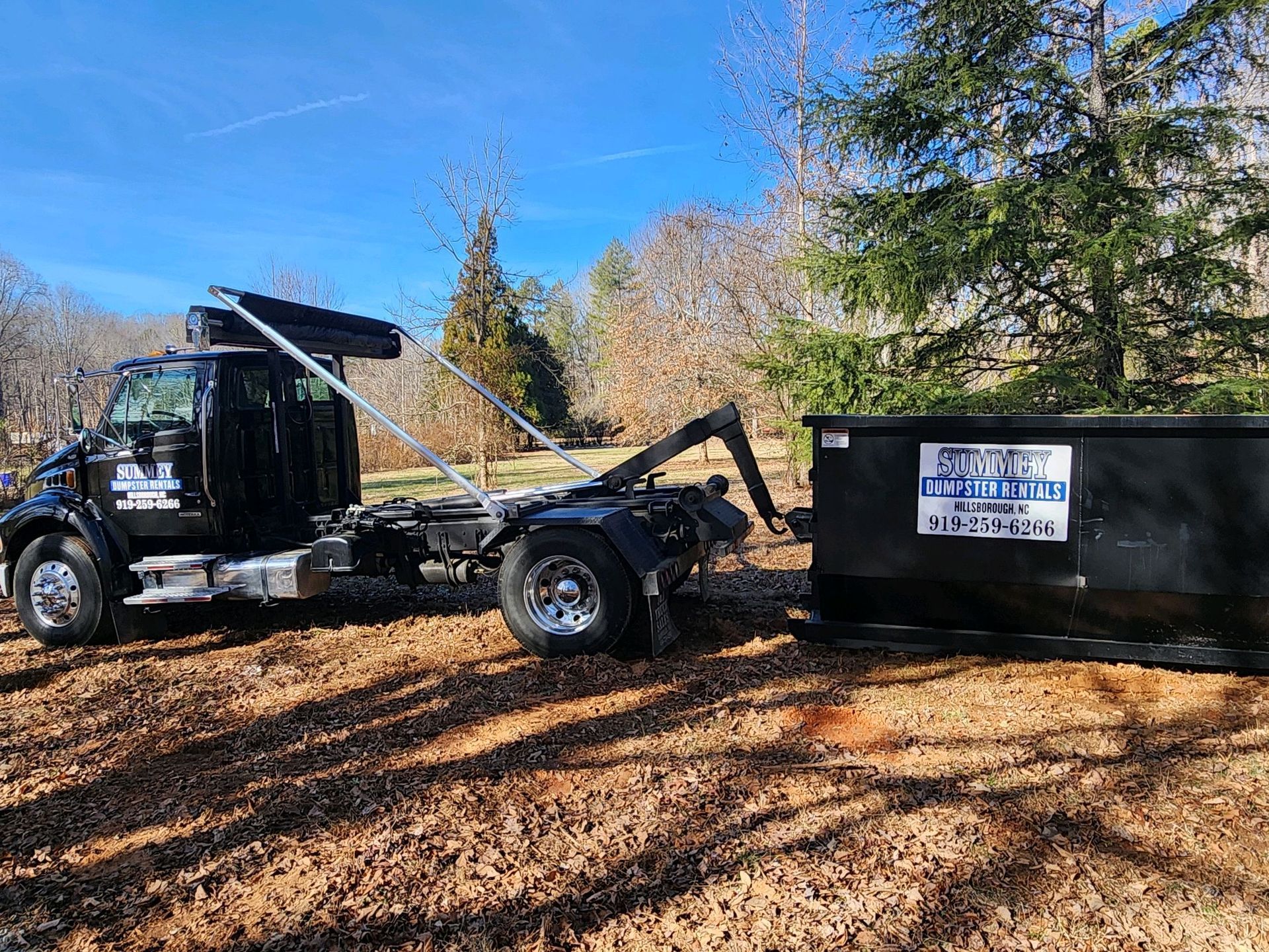 A dumpster is being towed by a dump truck.