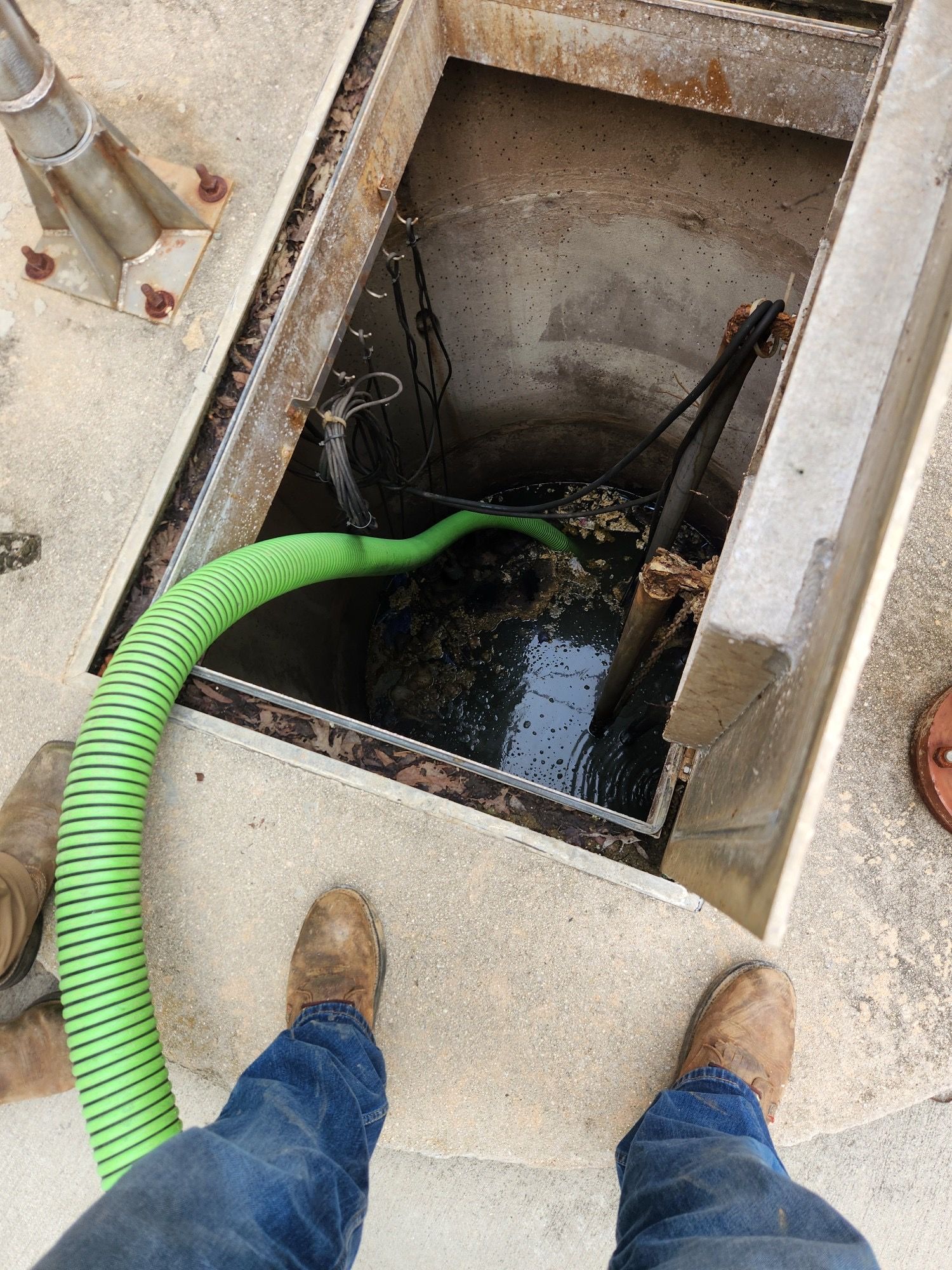A person is standing in a manhole with a green hose attached to it.