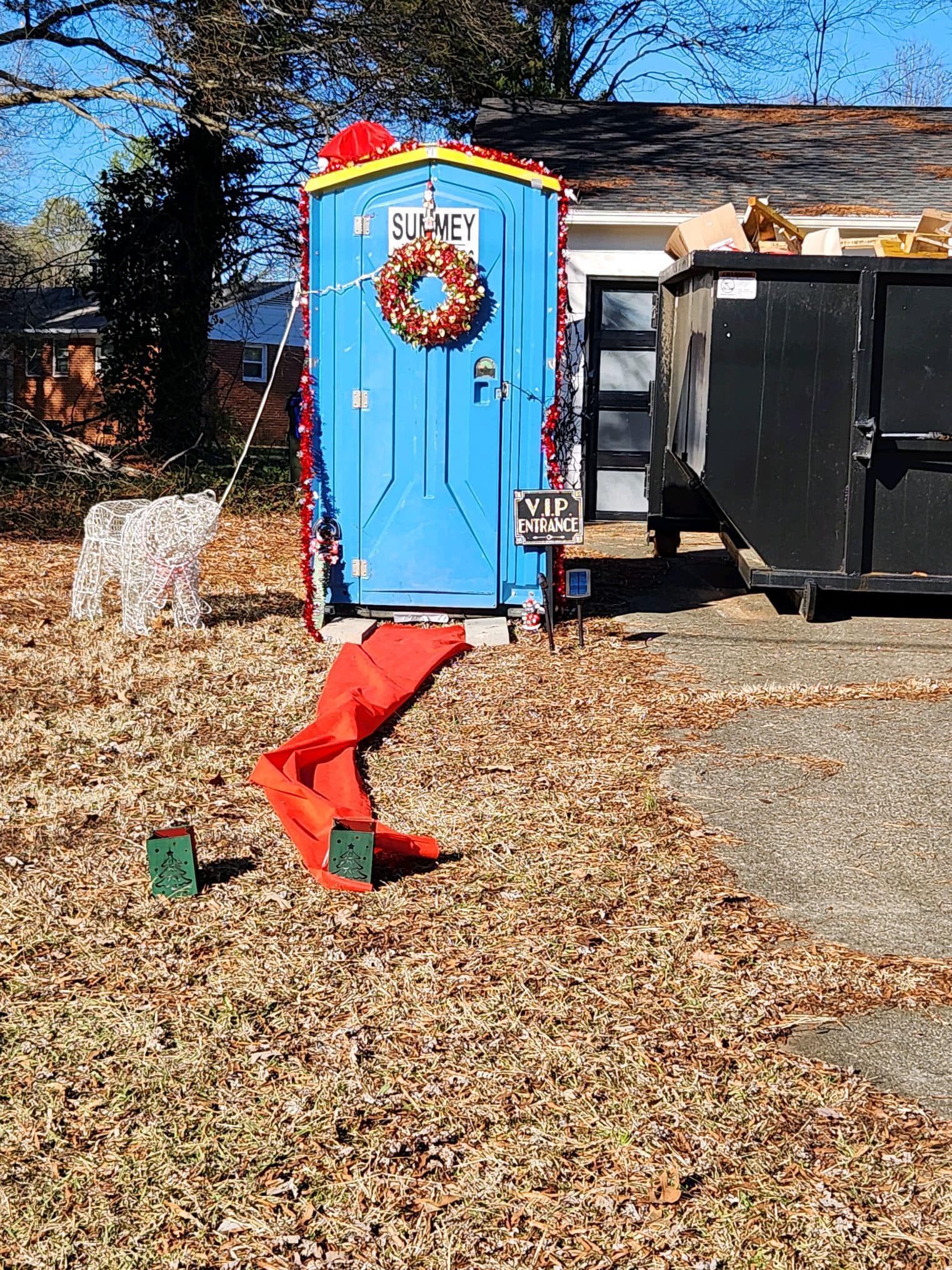 A blue portable toilet with a wreath on the door is decorated for christmas.