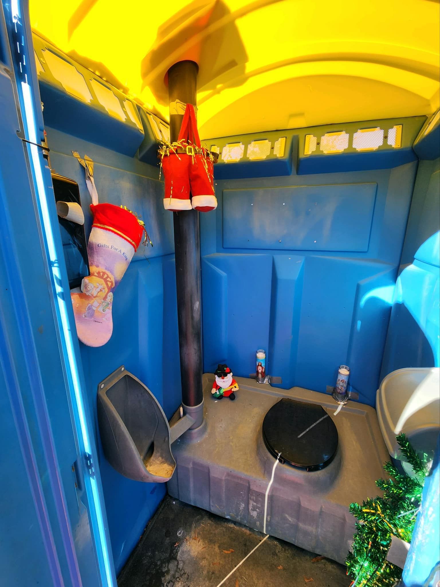 A portable toilet decorated for christmas with stockings hanging from the ceiling.