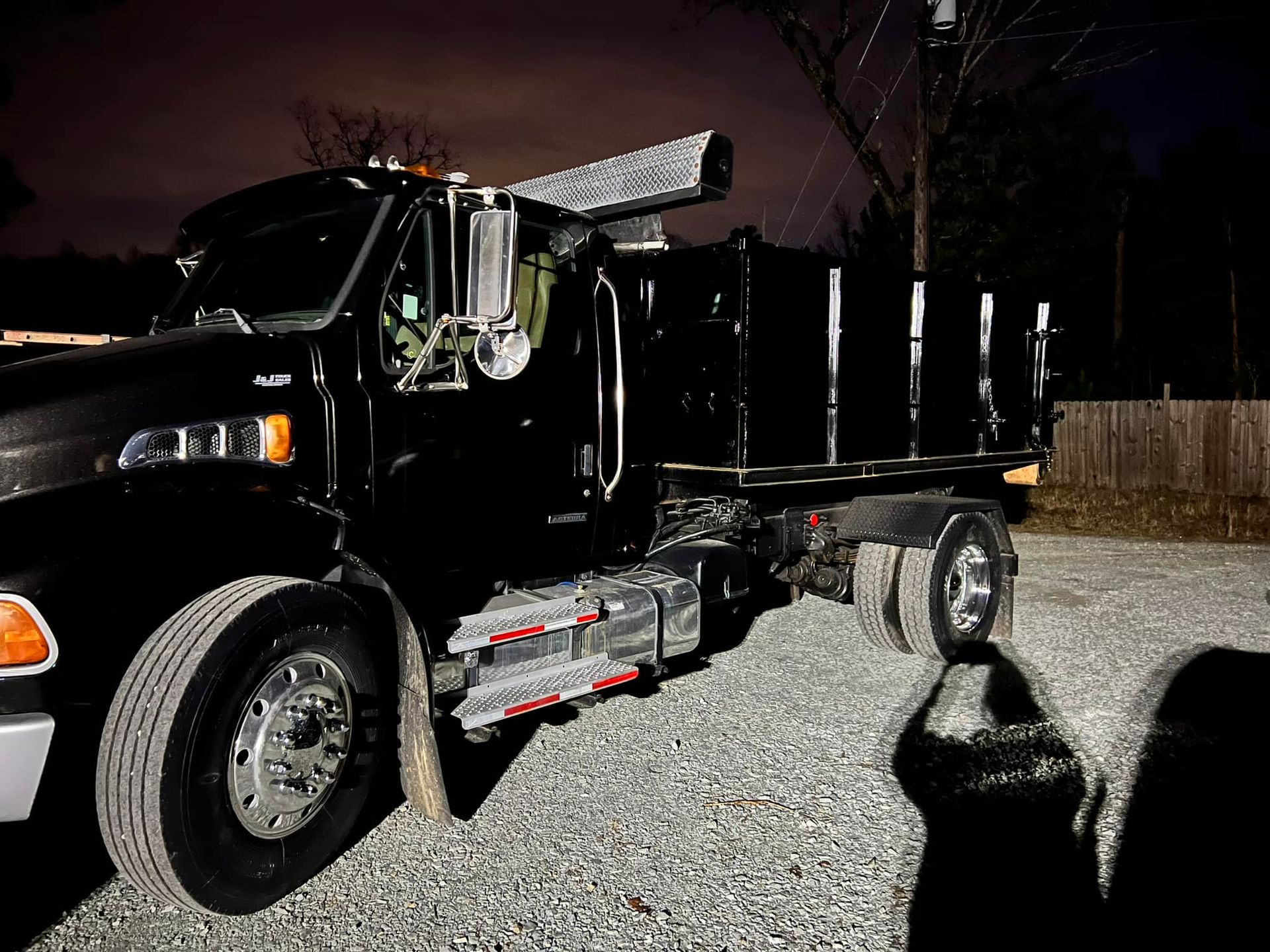 A black dump truck is parked in a gravel lot at night.