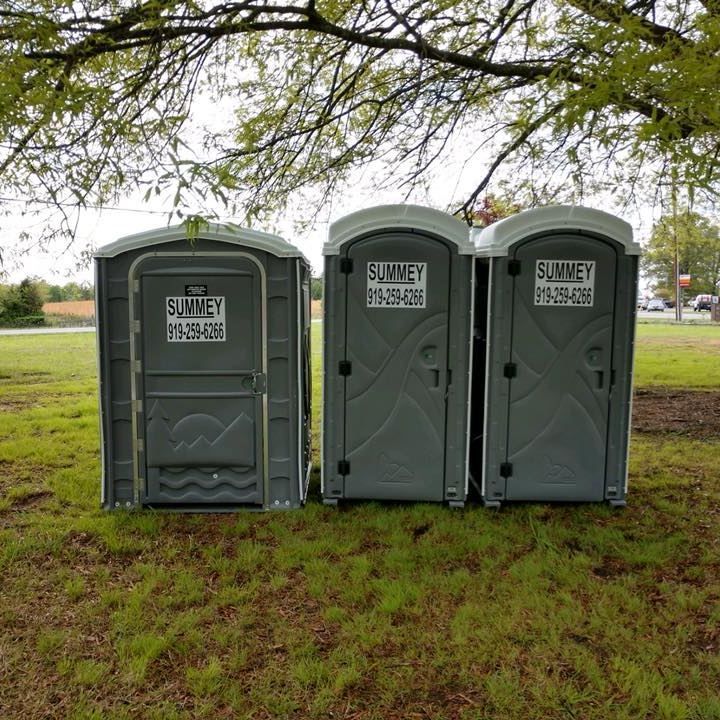 Three portable toilets are lined up in a grassy field.