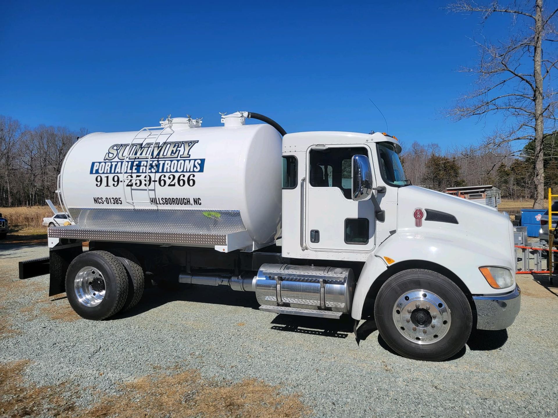 A white vacuum truck is parked in a gravel lot