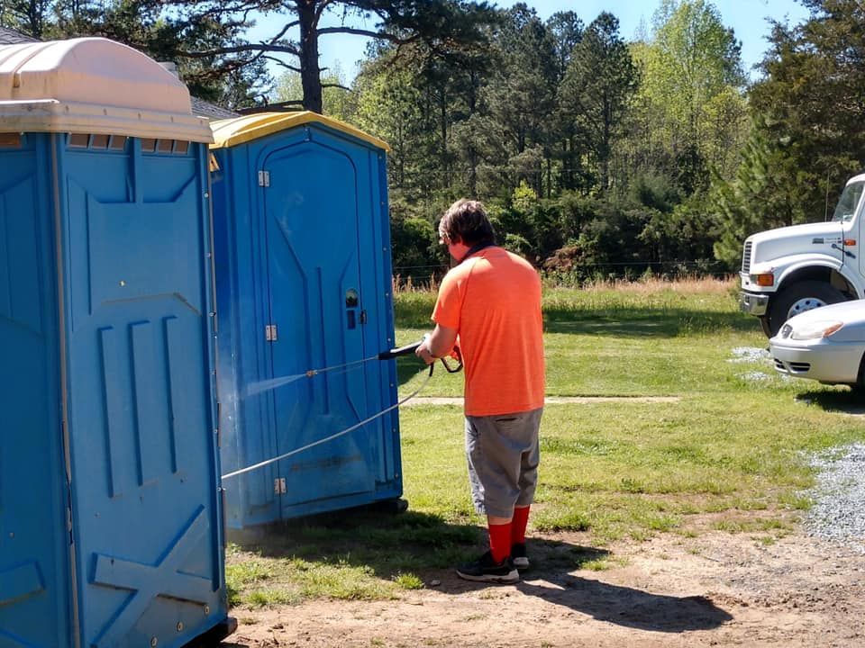 A man in an orange shirt is washing a blue portable toilet