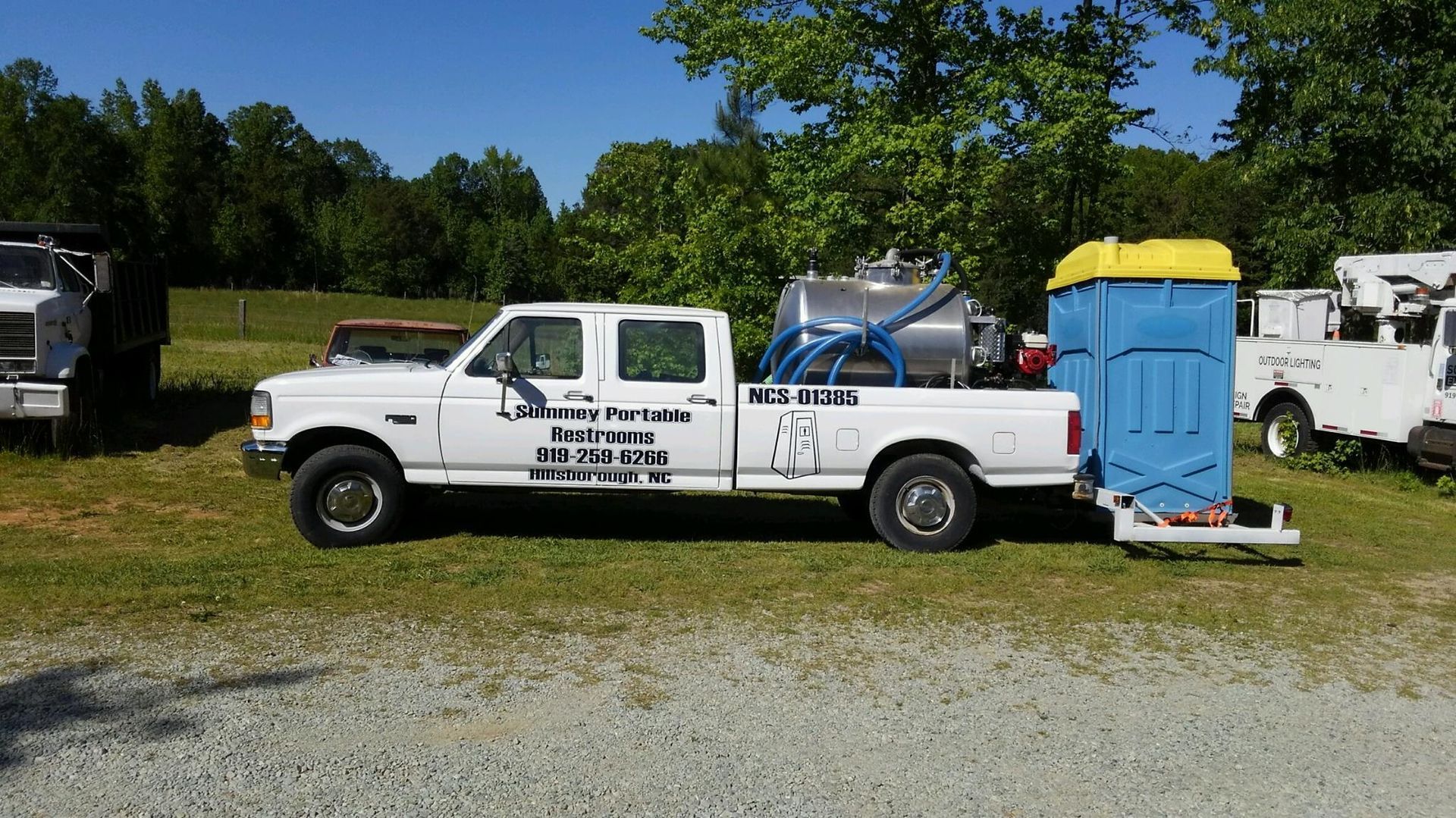 A white truck is parked next to a blue portable toilet.