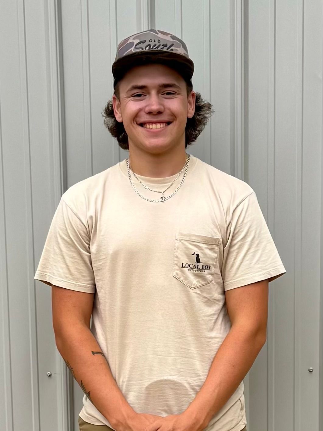 A young man wearing a hat and a t-shirt is standing in front of a metal wall.