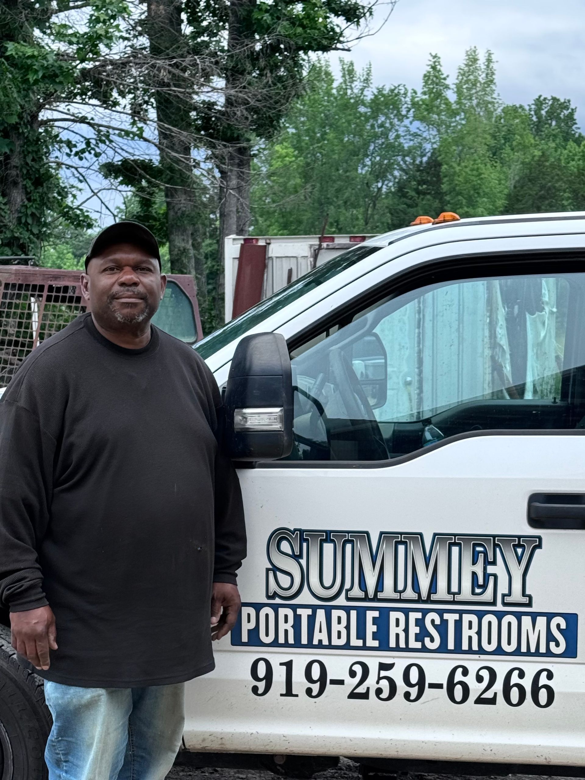 A man is standing in front of a white truck that says summery portable restrooms.