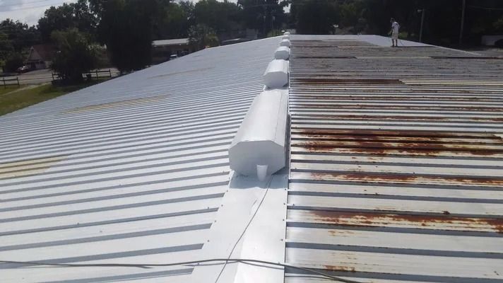 A metal roof with old, rusty sections being replaced with new, white metal.