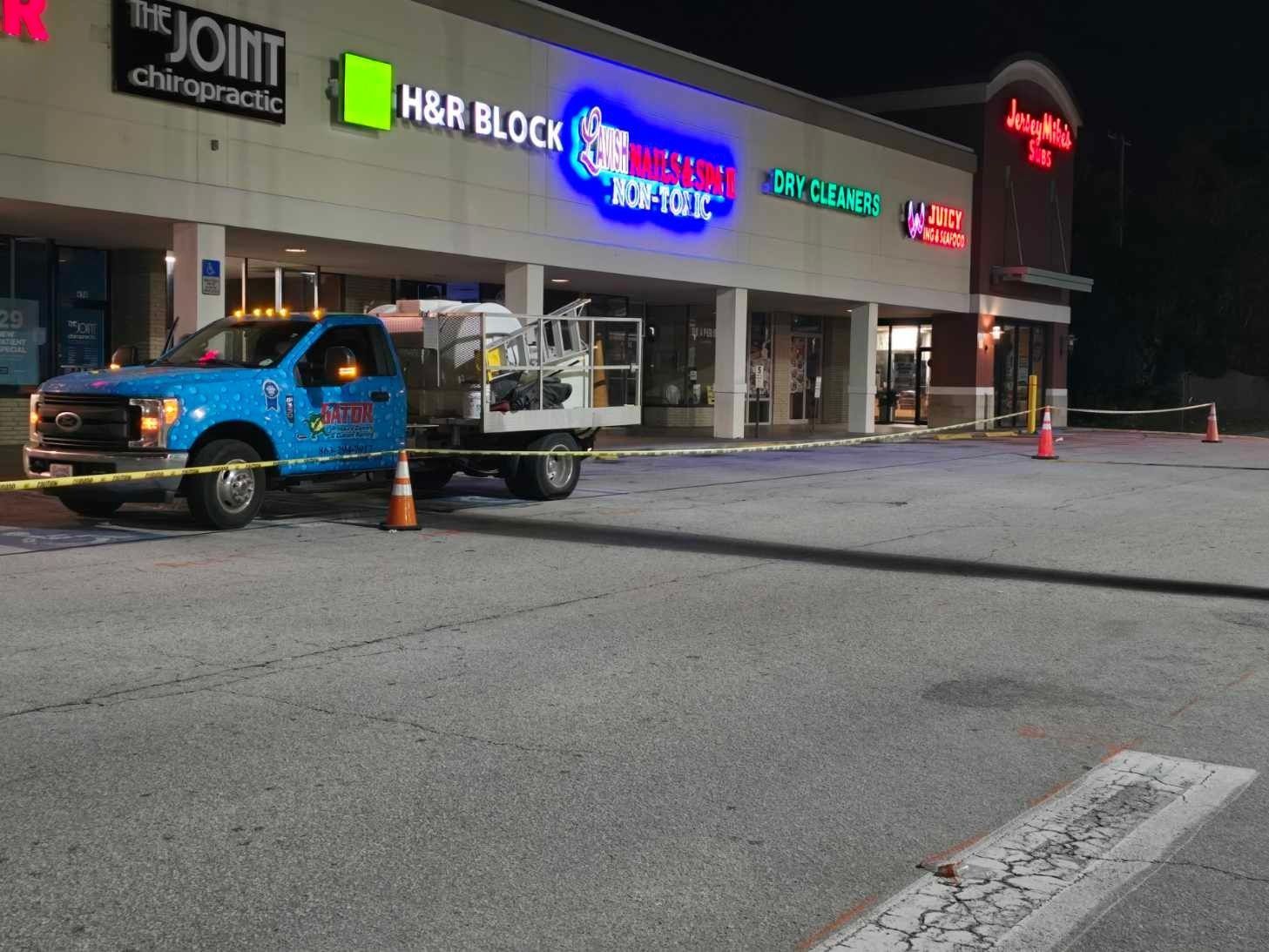 Blue truck parked in front of strip mall with caution tape. Businesses include The Joint Chiropractic, H&R Block, and dry cleaners.