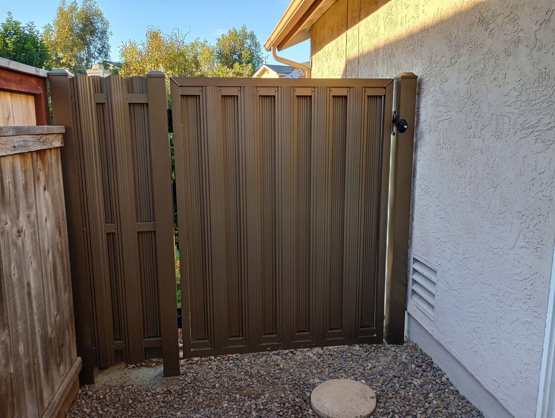 Wooden backyard gate beside a white stucco wall and gravel path