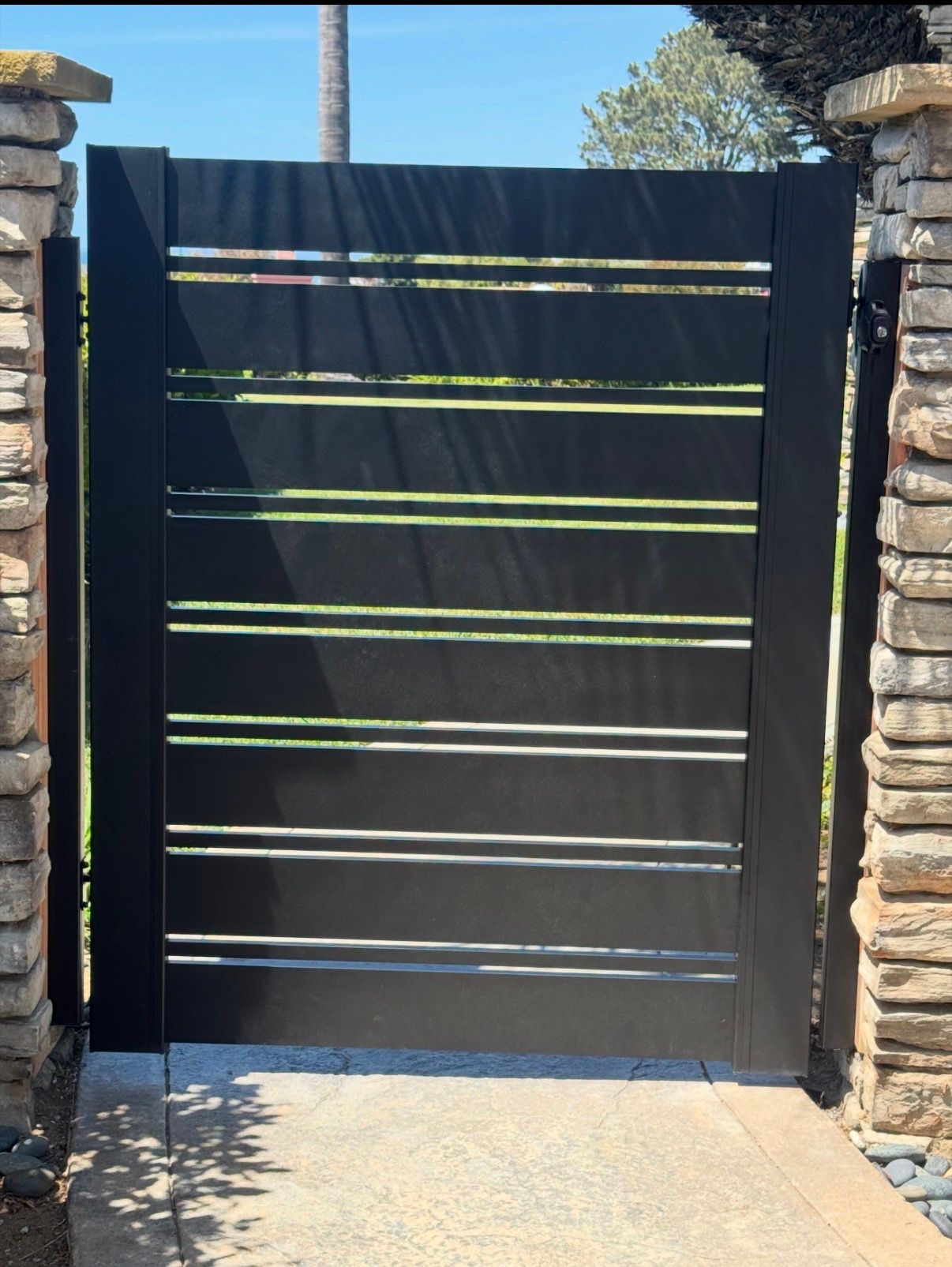 Black slatted gate between stone pillars in bright sunlight