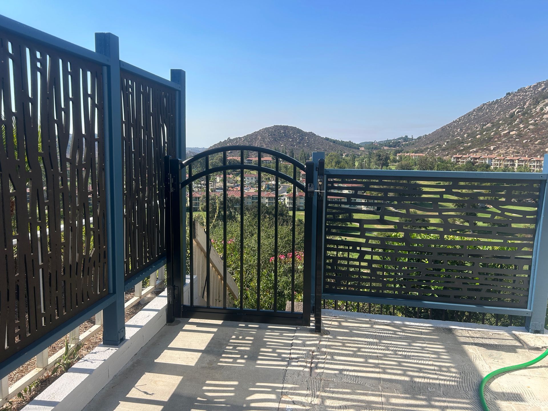 Patio gate and railing overlooking a hillside neighborhood in bright sunlight