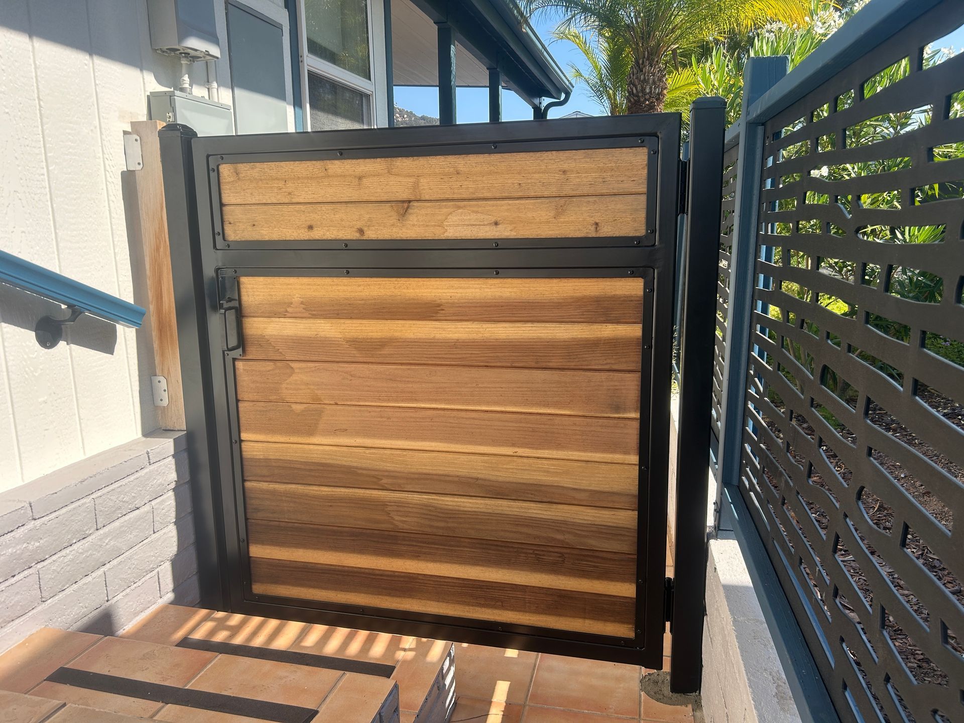 Wooden gate blocking a narrow side passage between a house and fence in bright sunlight