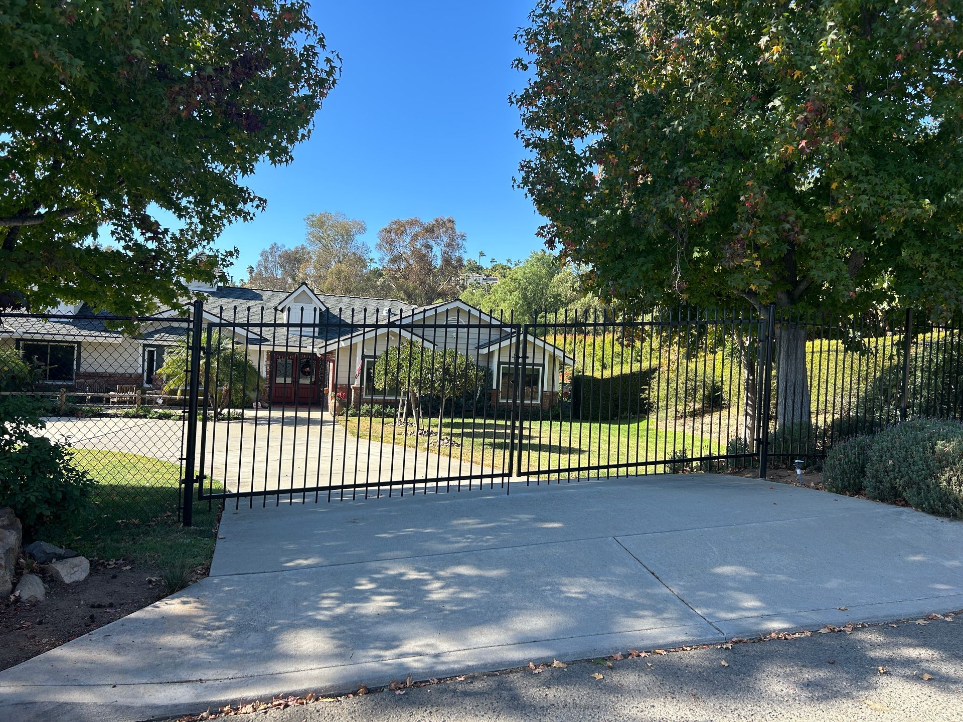 Driveway leading to a closed black metal gate between trees and a house in the background