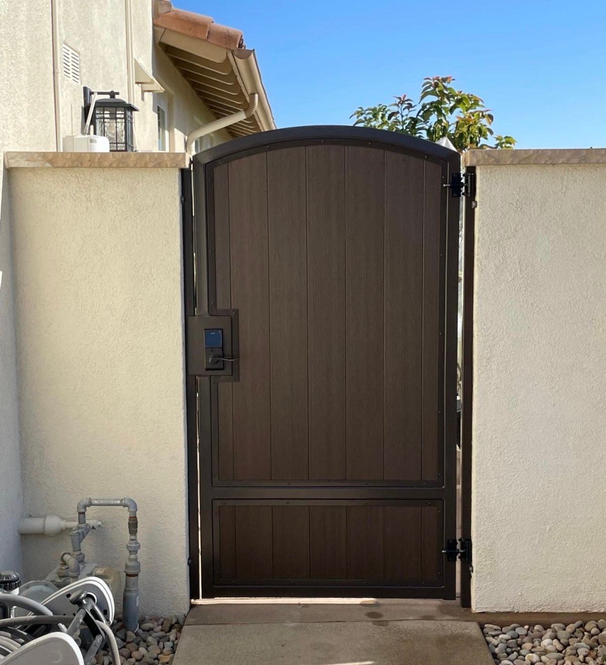 Brown arched wooden gate set in a stucco wall with a house and bicycles beside it