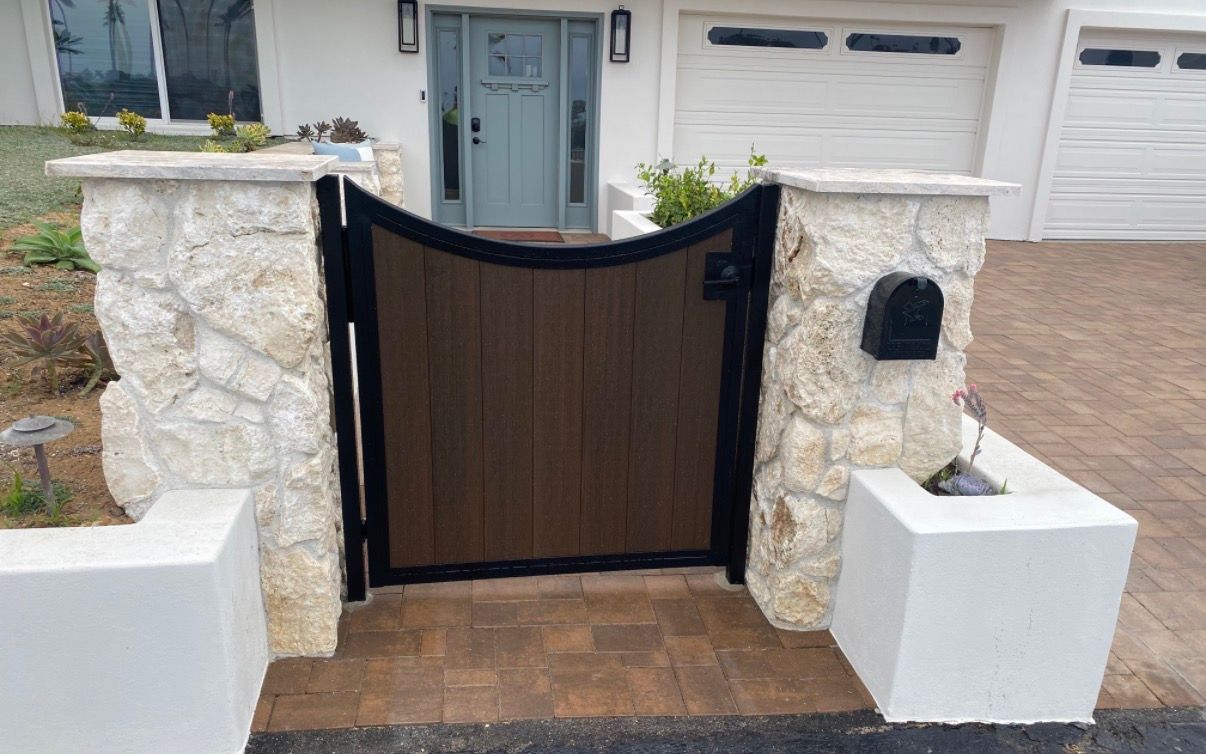 Front yard gate with black and brown wood panels between stone pillars and white planters.