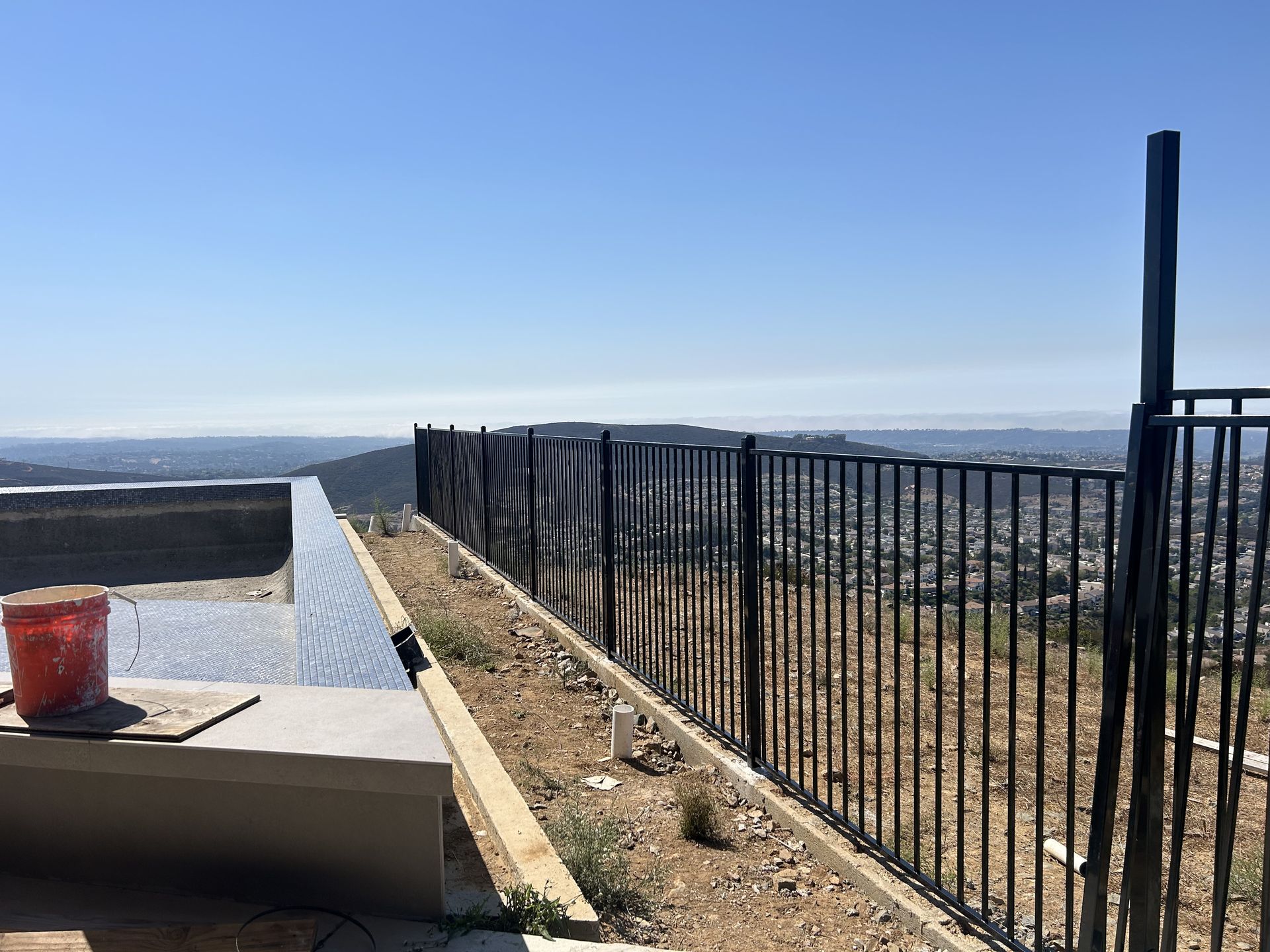Rooftop terrace with black railing, concrete ledge, and distant city view under a clear blue sky