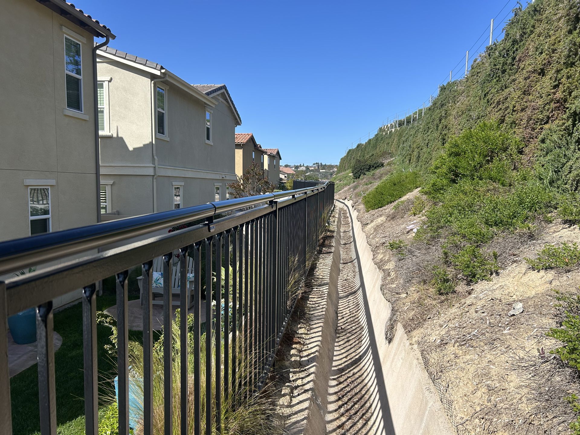 Railing-lined path beside houses and a rocky hillside under a bright blue sky