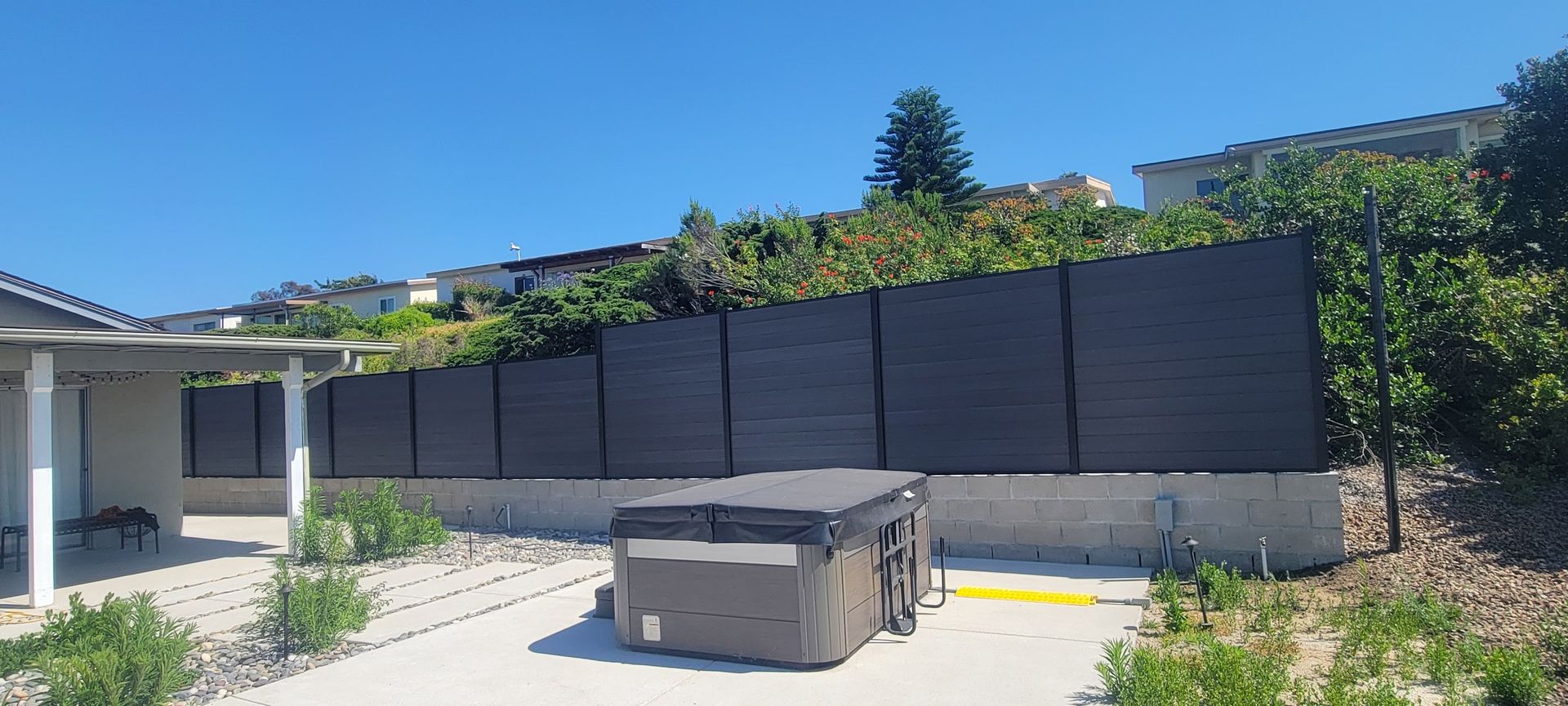 Backyard patio with a gray hot tub, concrete slab, and dark fence under bright sunlight