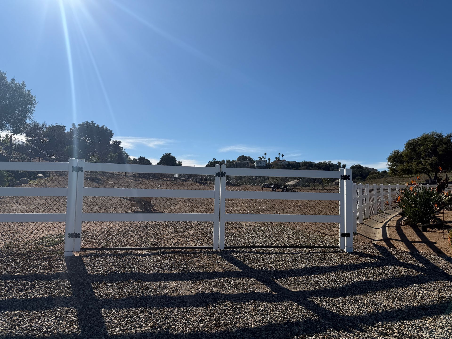 White ranch fence beside a gravel path under a clear blue sky
