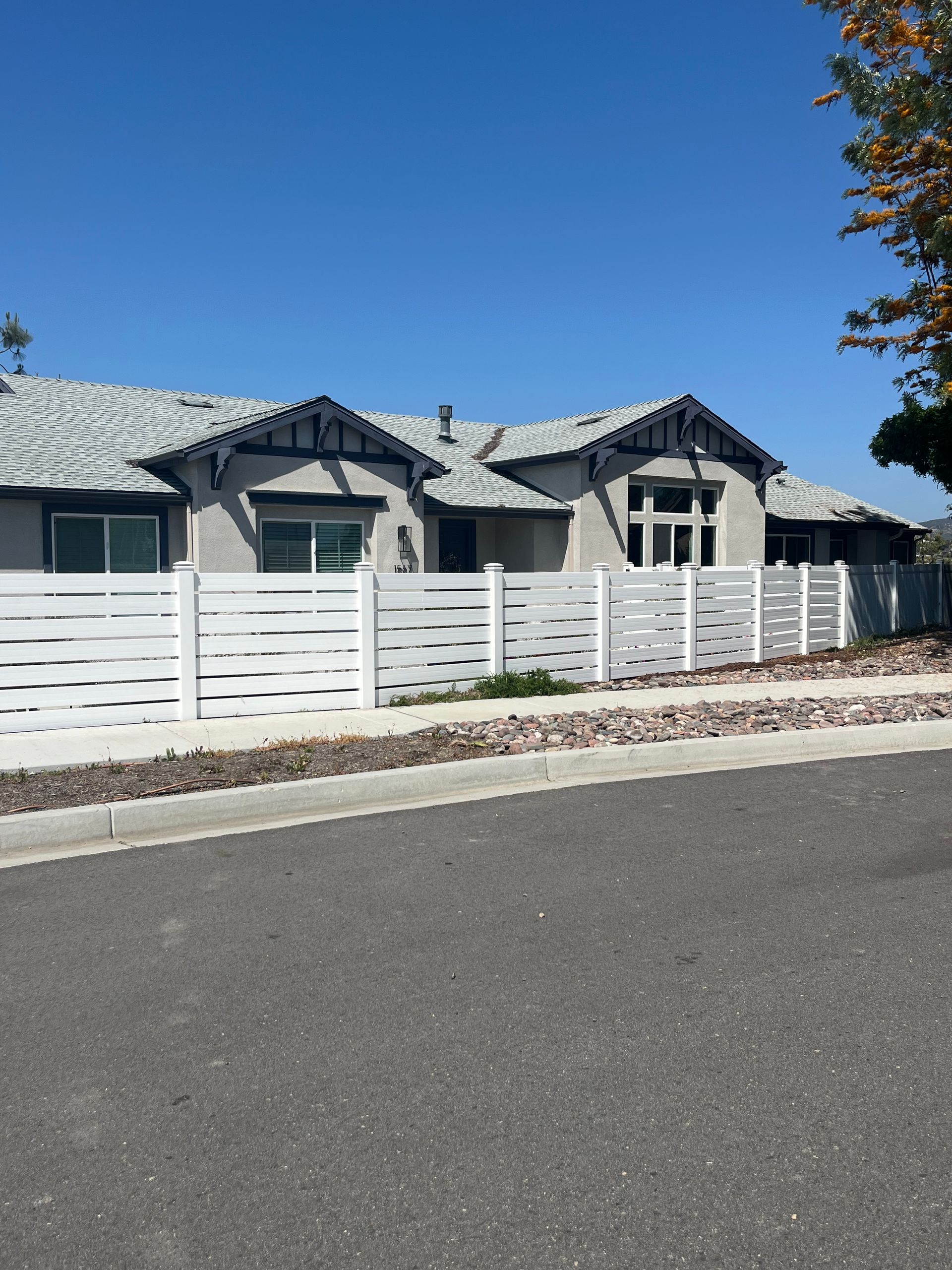 Single-story suburban house with a white fence and blue roof under a clear sky