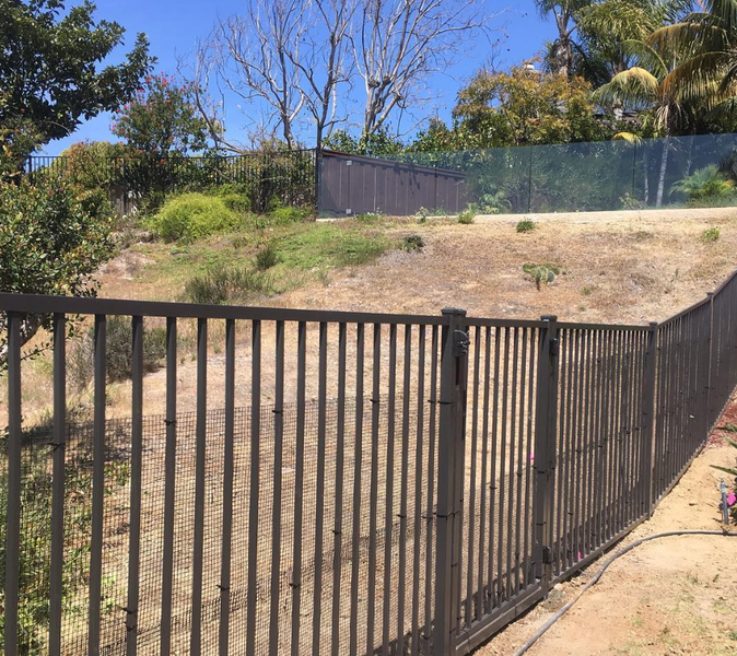 A black metal fence surrounds a dirt field with trees in the background.