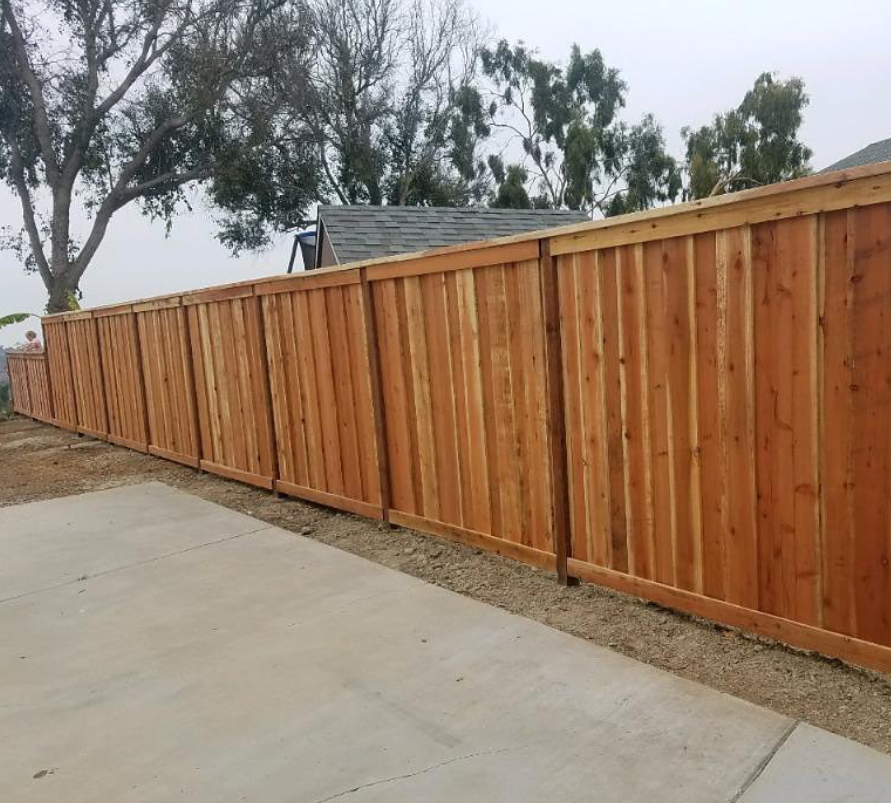 A wooden fence is sitting next to a concrete driveway.