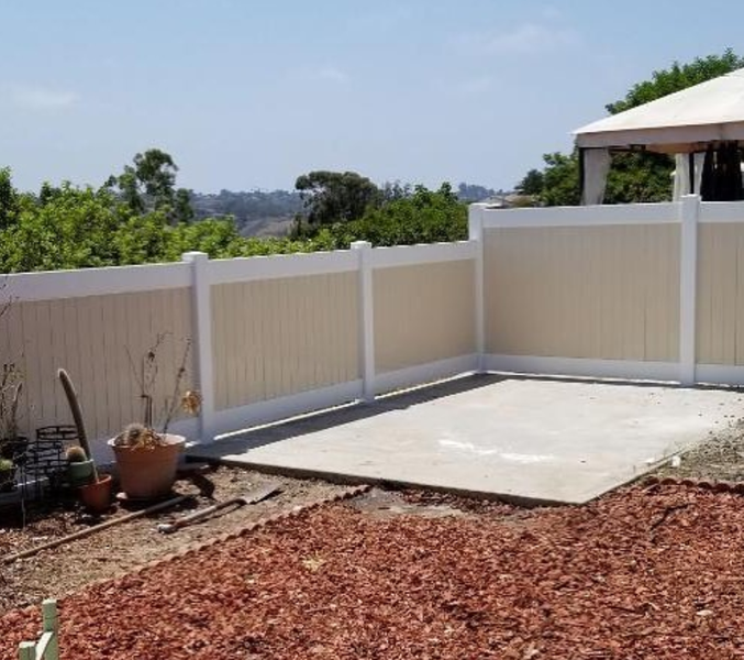 A white fence surrounds a concrete area in a backyard