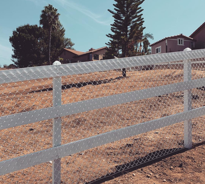 A white fence surrounds a dirt field with houses in the background