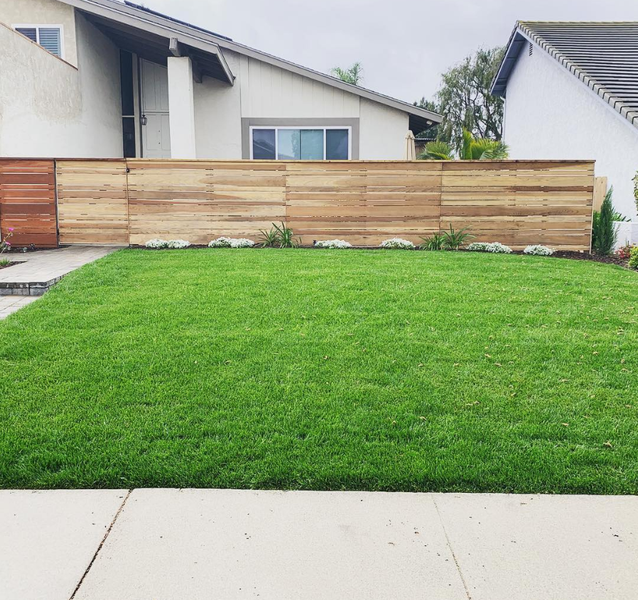 A lush green lawn in front of a house with a wooden fence