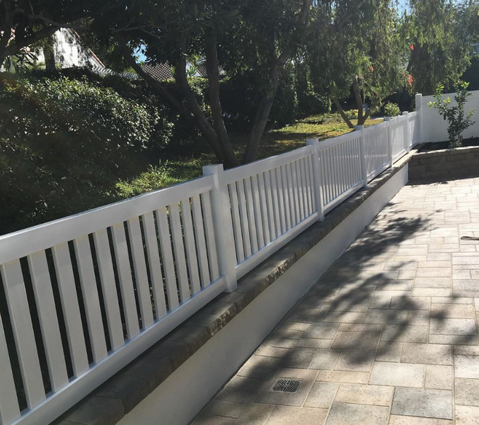 A white fence surrounds a patio with trees in the background