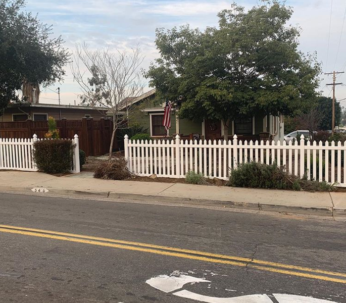 A white picket fence surrounds a house on the side of the road.