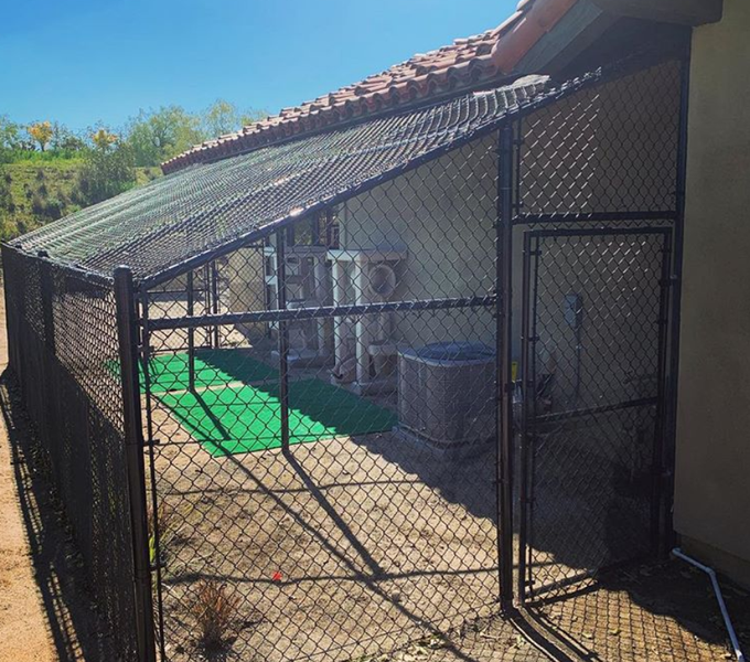 A chain link fence surrounds a building with a green mat