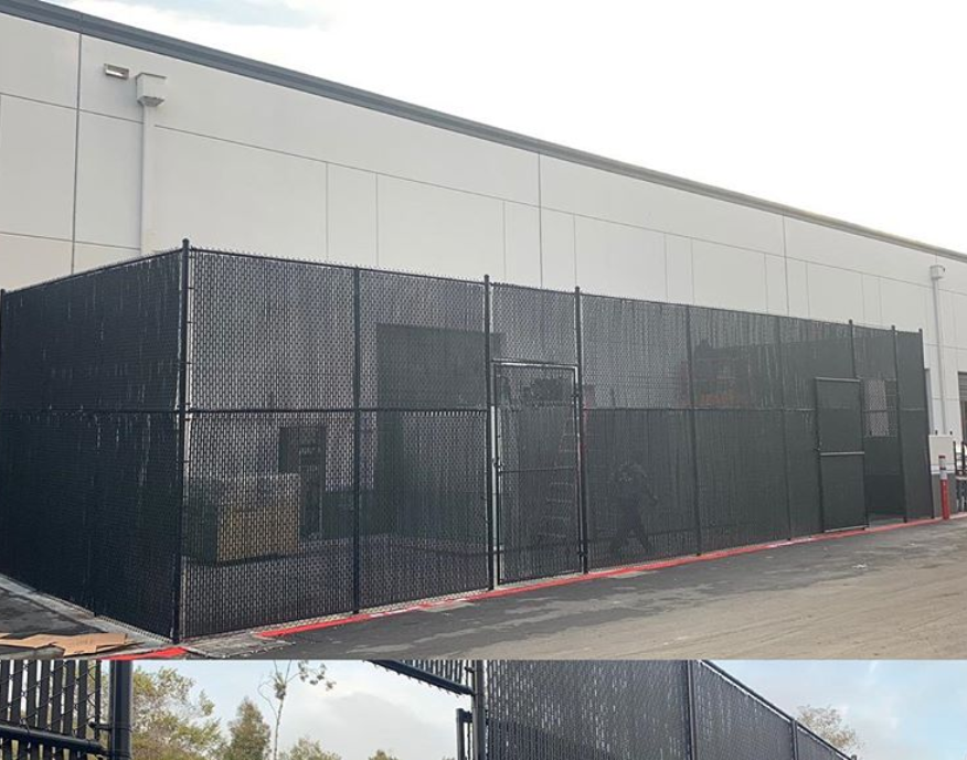 A black chain link fence is surrounding a large building.