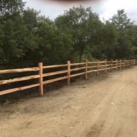 A wooden fence along a dirt road with trees in the background.