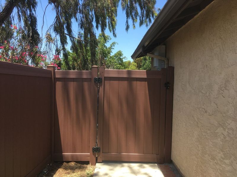 A brown fence is surrounding a house with trees in the background.